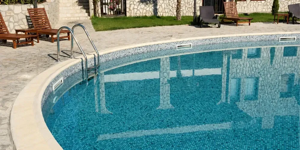 Outdoor swimming pool with clear blue water, curved edge, ladder, and lounge chairs nearby