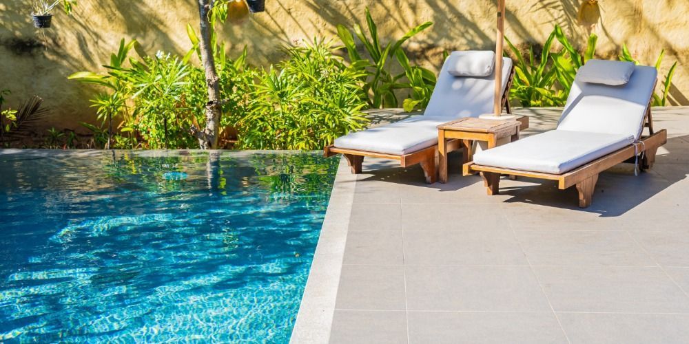 Poolside lounge chairs beside a blue swimming pool with tropical greenery