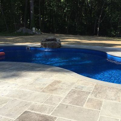 A large swimming pool surrounded by trees and a tiled patio.