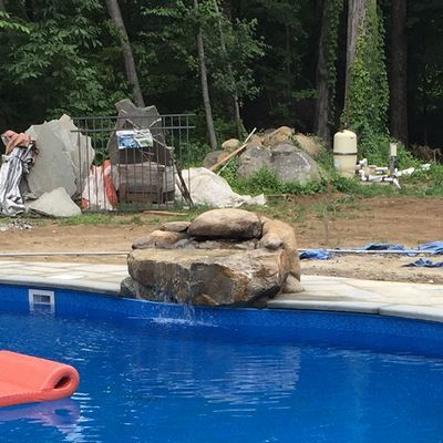 A large rock is sitting on the edge of a swimming pool.