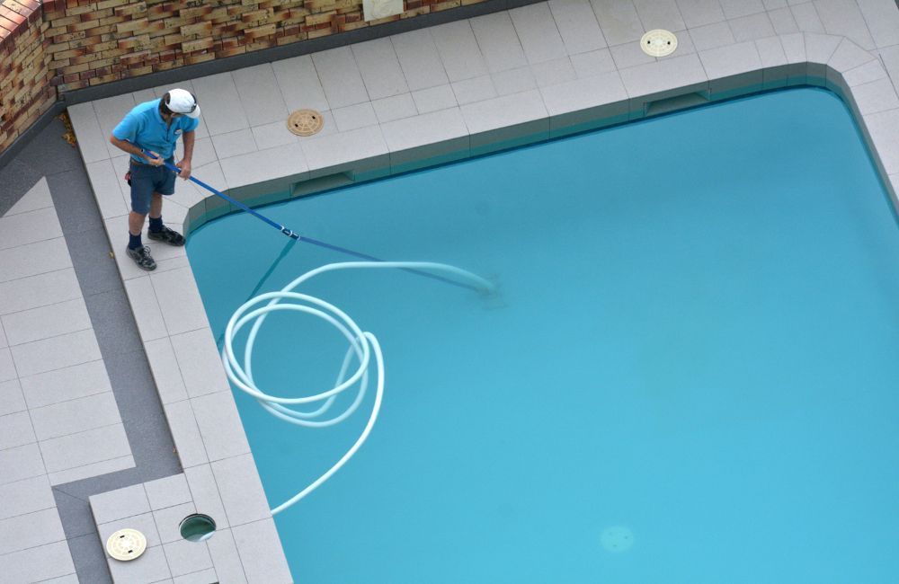 A man is cleaning a swimming pool with a hose