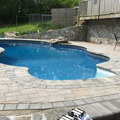 A large swimming pool is surrounded by bricks and a stone wall.