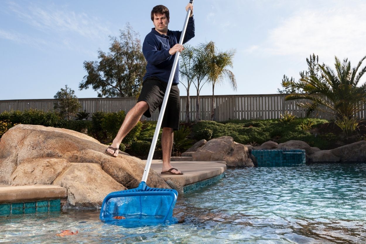 A man is cleaning a swimming pool with a rake.