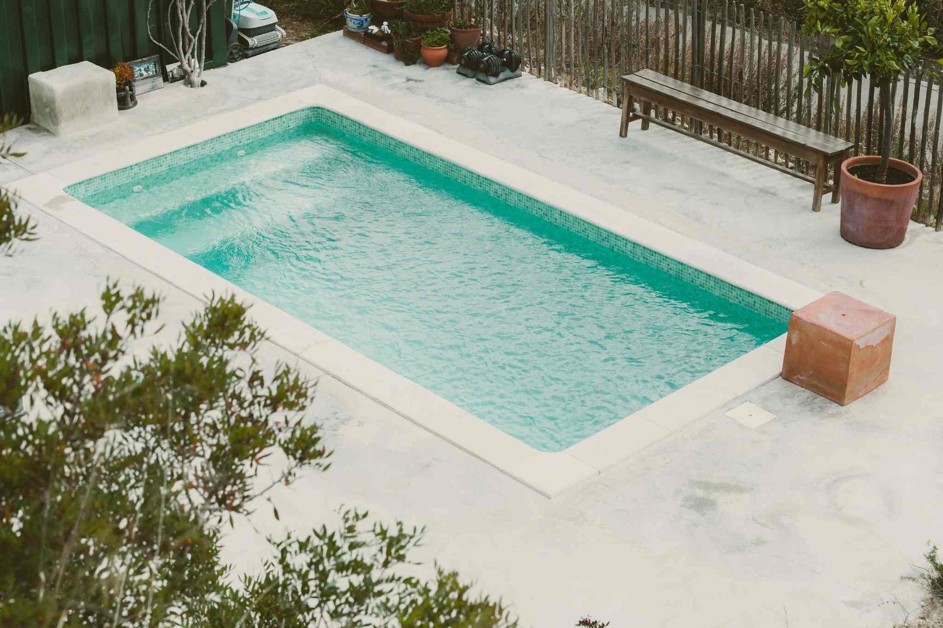 A swimming pool with a bench and potted plants around it