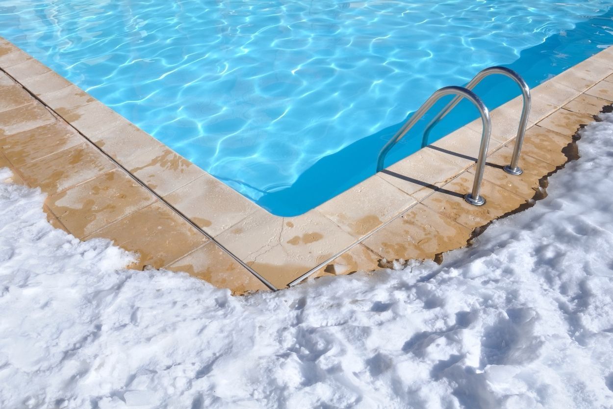 A swimming pool covered in snow with stairs leading to it