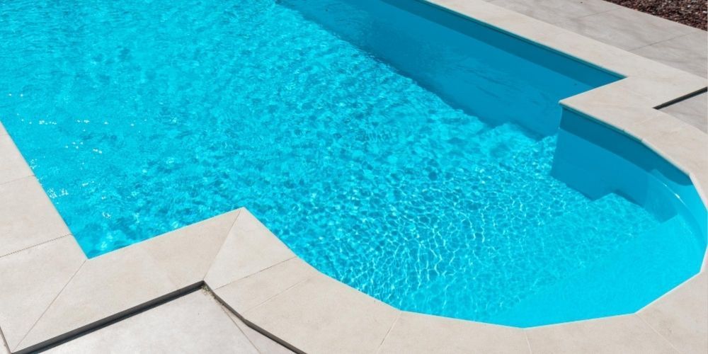 Bright turquoise swimming pool with white stone deck and blue-tiled edges