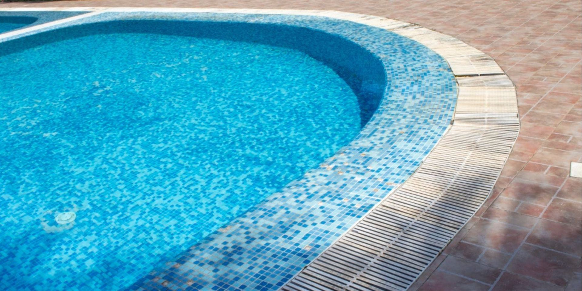 Curved swimming pool edge with blue mosaic tiles and brick deck under bright sunlight