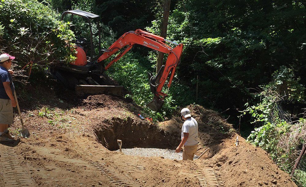A man is digging a hole in the dirt next to an excavator.