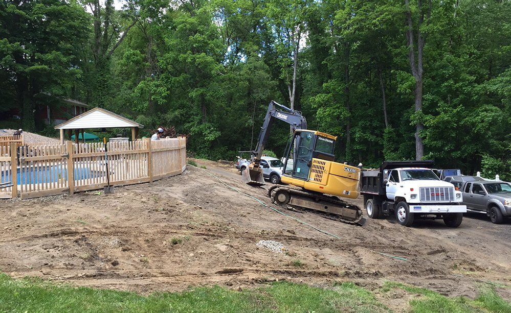 A large yellow excavator is sitting on top of a dirt field next to a dump truck.