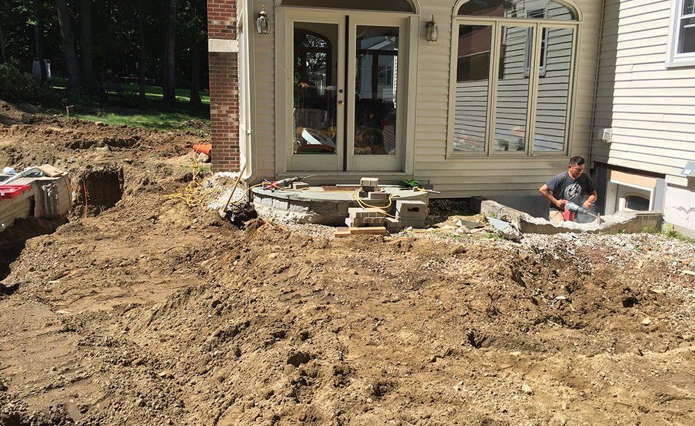 A man is sitting in the dirt in front of a house.