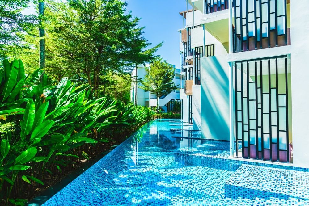 A large swimming pool in the middle of a lush green garden next to a building.