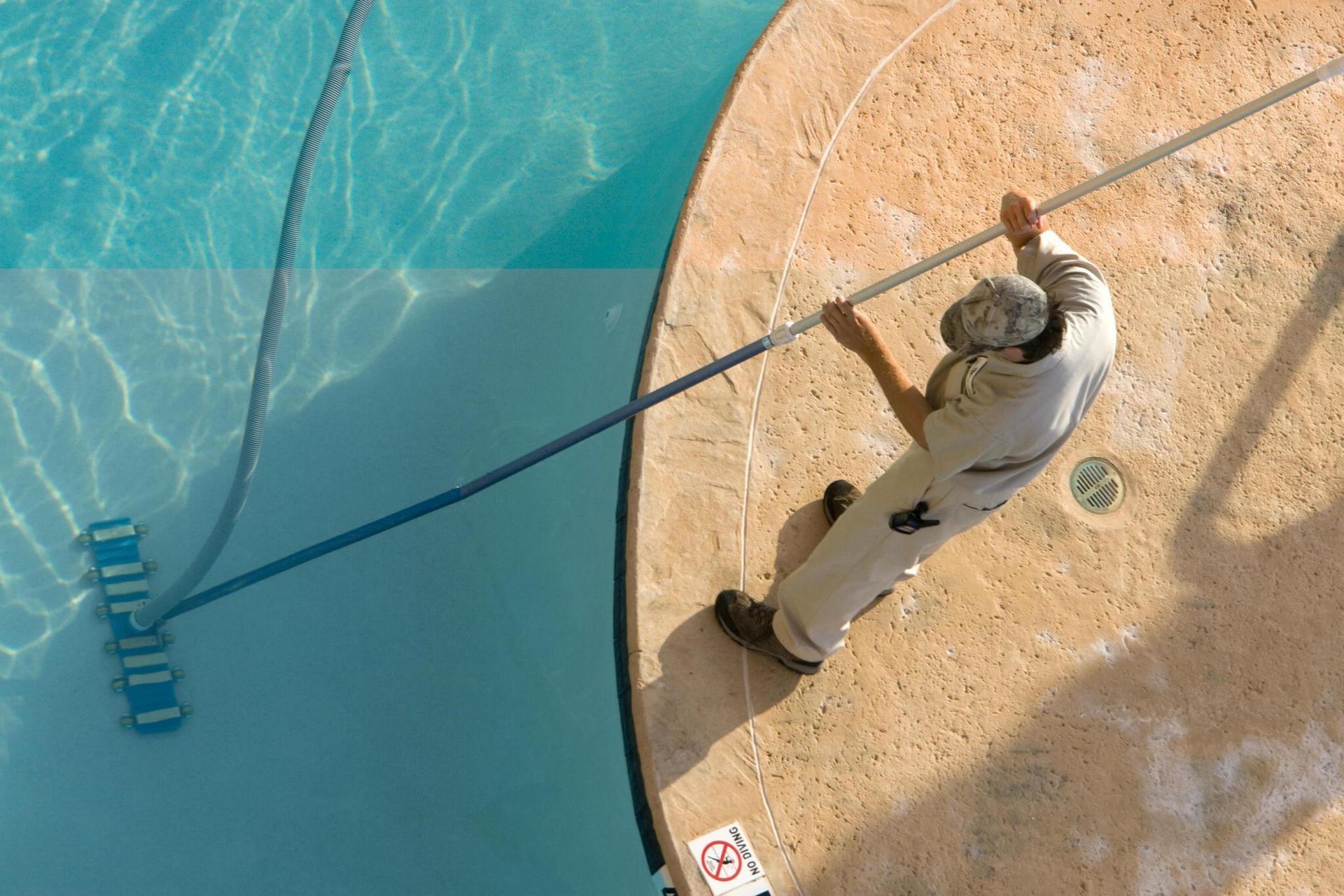 A man is cleaning a swimming pool with a broom.