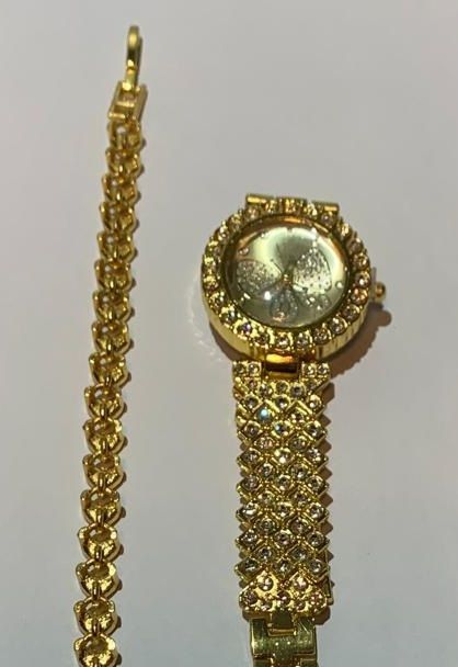 Een gouden horloge en armband liggen op een wit oppervlak