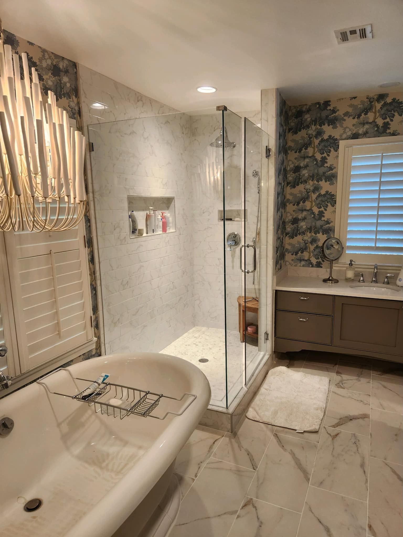 Bathroom with a white clawfoot tub, glass shower, and patterned wallpaper.