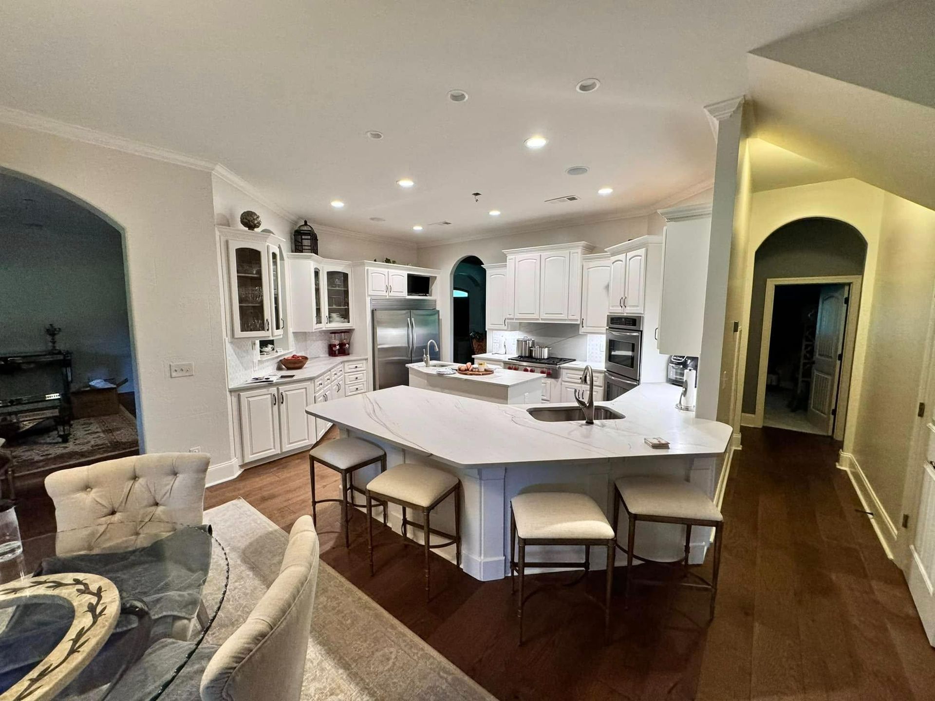 White kitchen with island, cabinets, and dining area; dark wood floors.