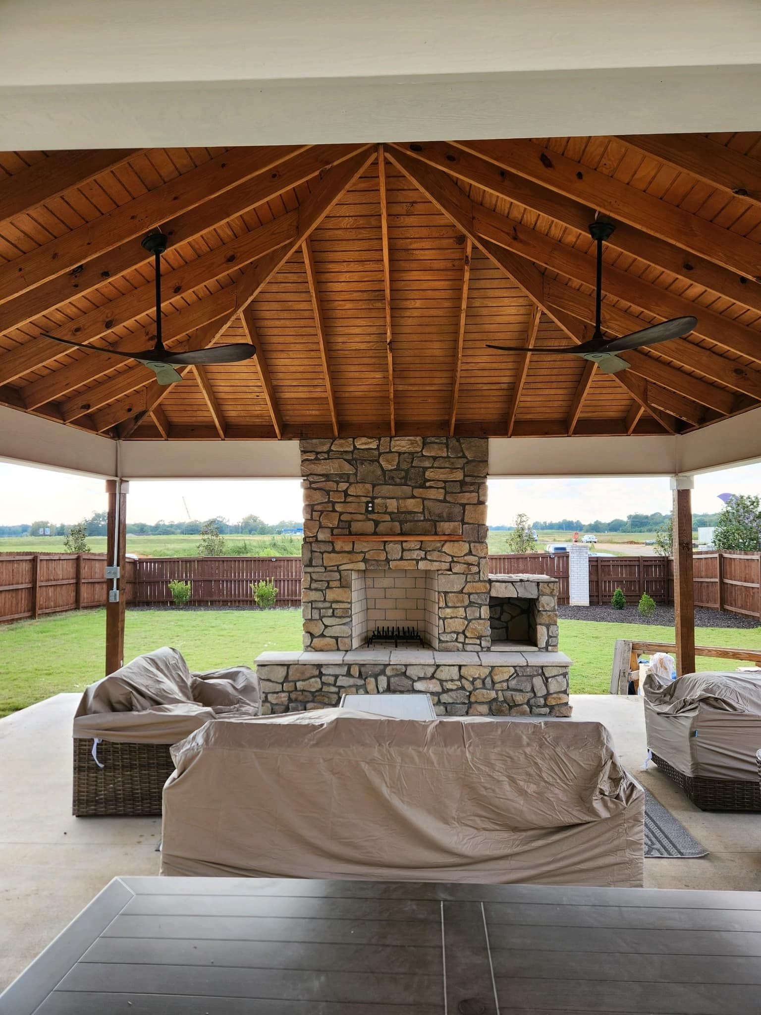 Outdoor patio with stone fireplace, wood ceiling, and covered furniture.