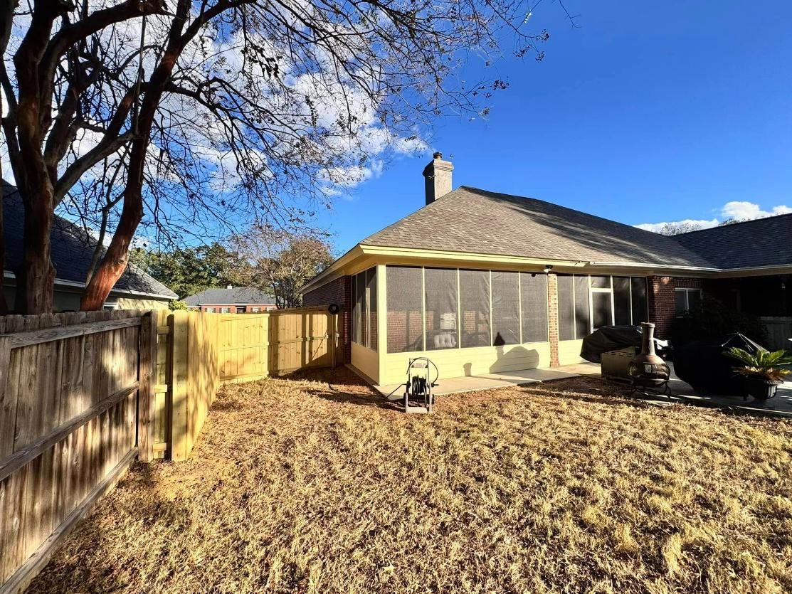Backyard view of a house with a screened-in porch, brown grass, and a wooden fence on a sunny day.