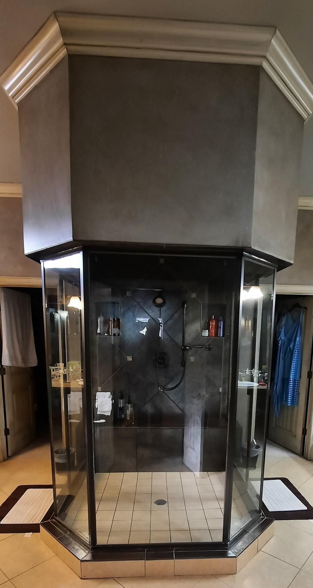 Octagonal glass shower with chrome trim and gray walls. White molding at top.
