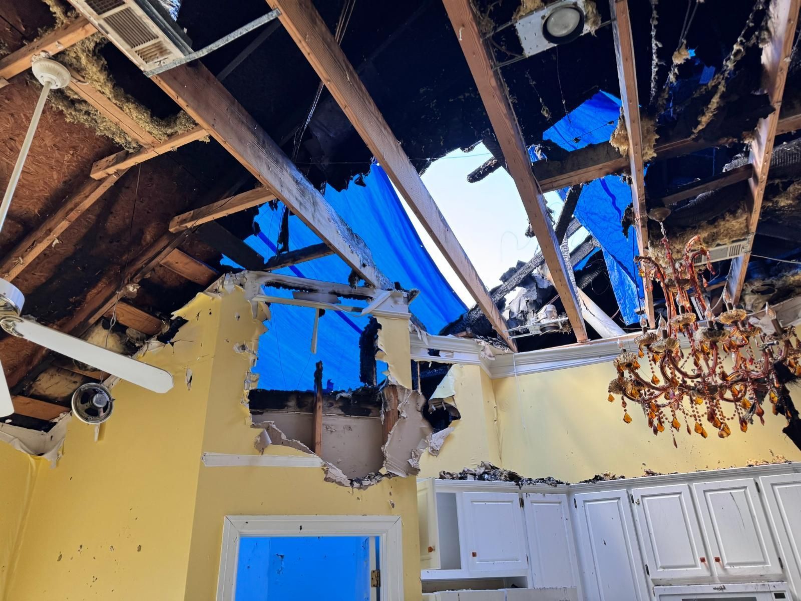 Interior view of a damaged building. A blue tarp covers the hole in the roof, yellow walls, and a hanging chandelier.