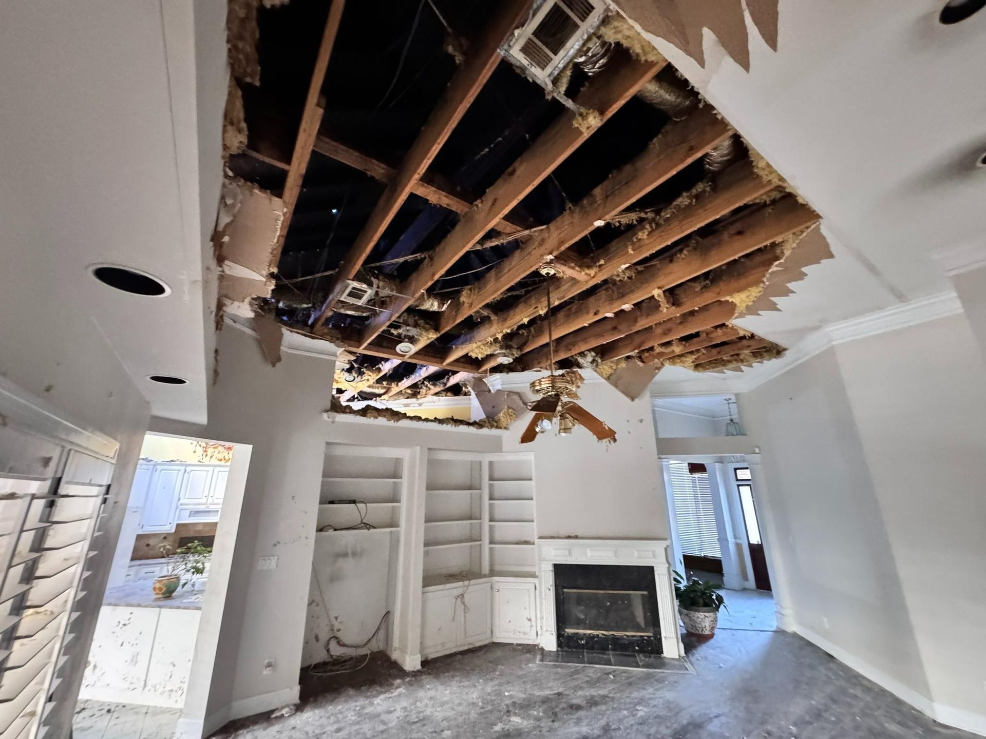 Damaged interior of a room, gaping hole in the ceiling exposing wood beams.