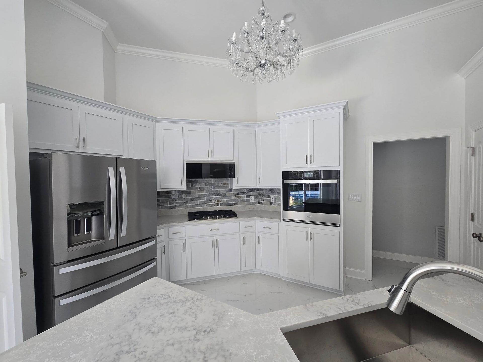 White kitchen with stainless steel appliances and a chandelier.
