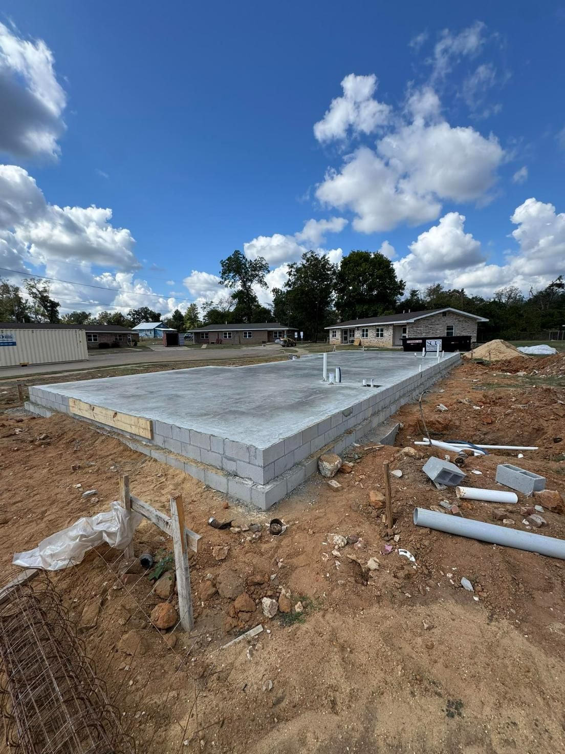 Concrete block foundation for a building under construction, on a brown dirt lot under a cloudy blue sky.