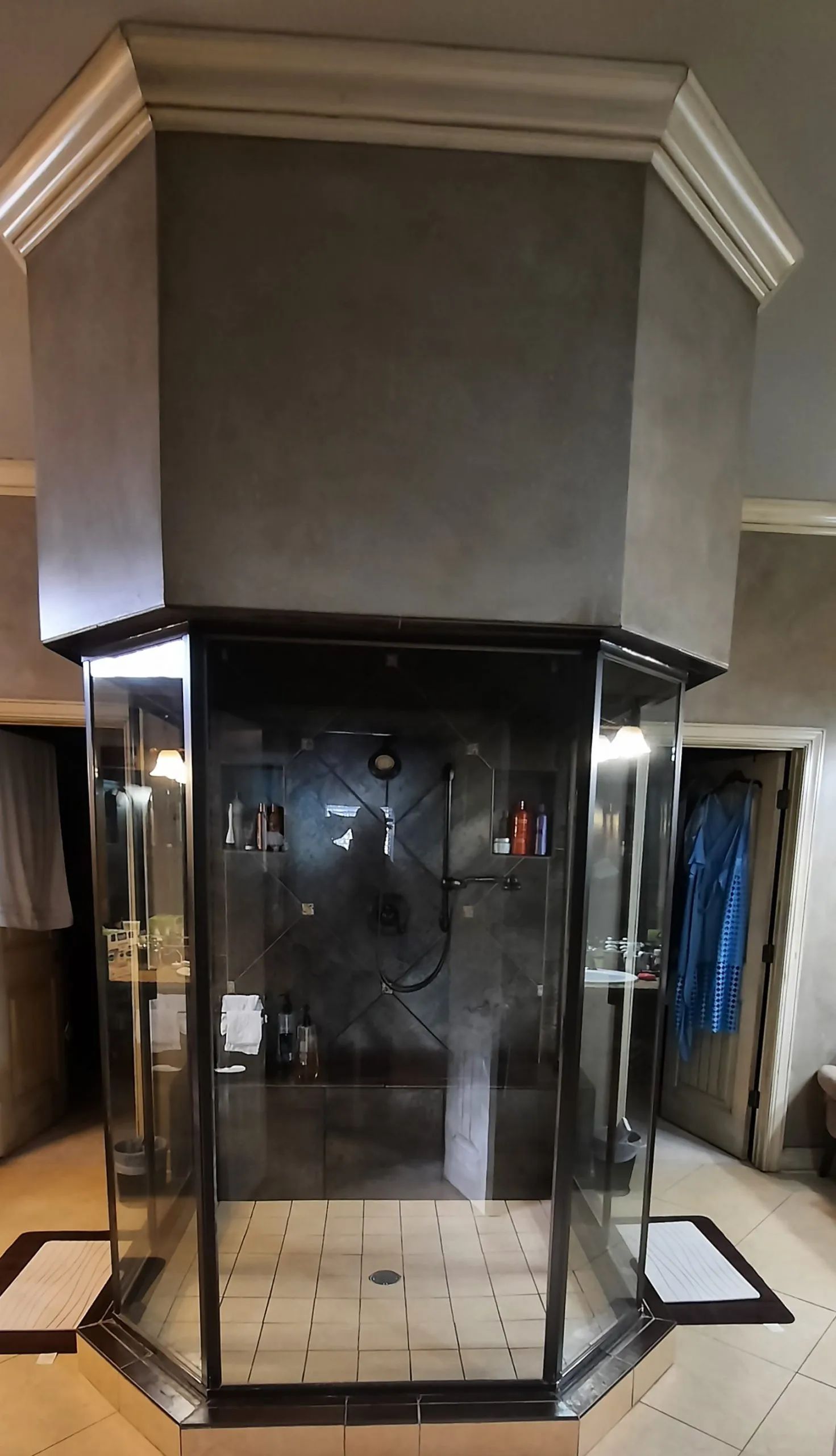 An octagonal shower enclosure with black metal framing and glass panels. Gray walls and white trim.