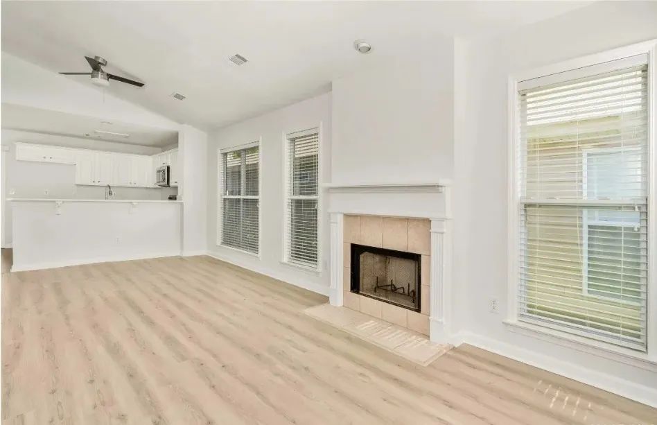 Empty living room with fireplace, three windows, and light wood-look flooring. White walls and cabinetry.