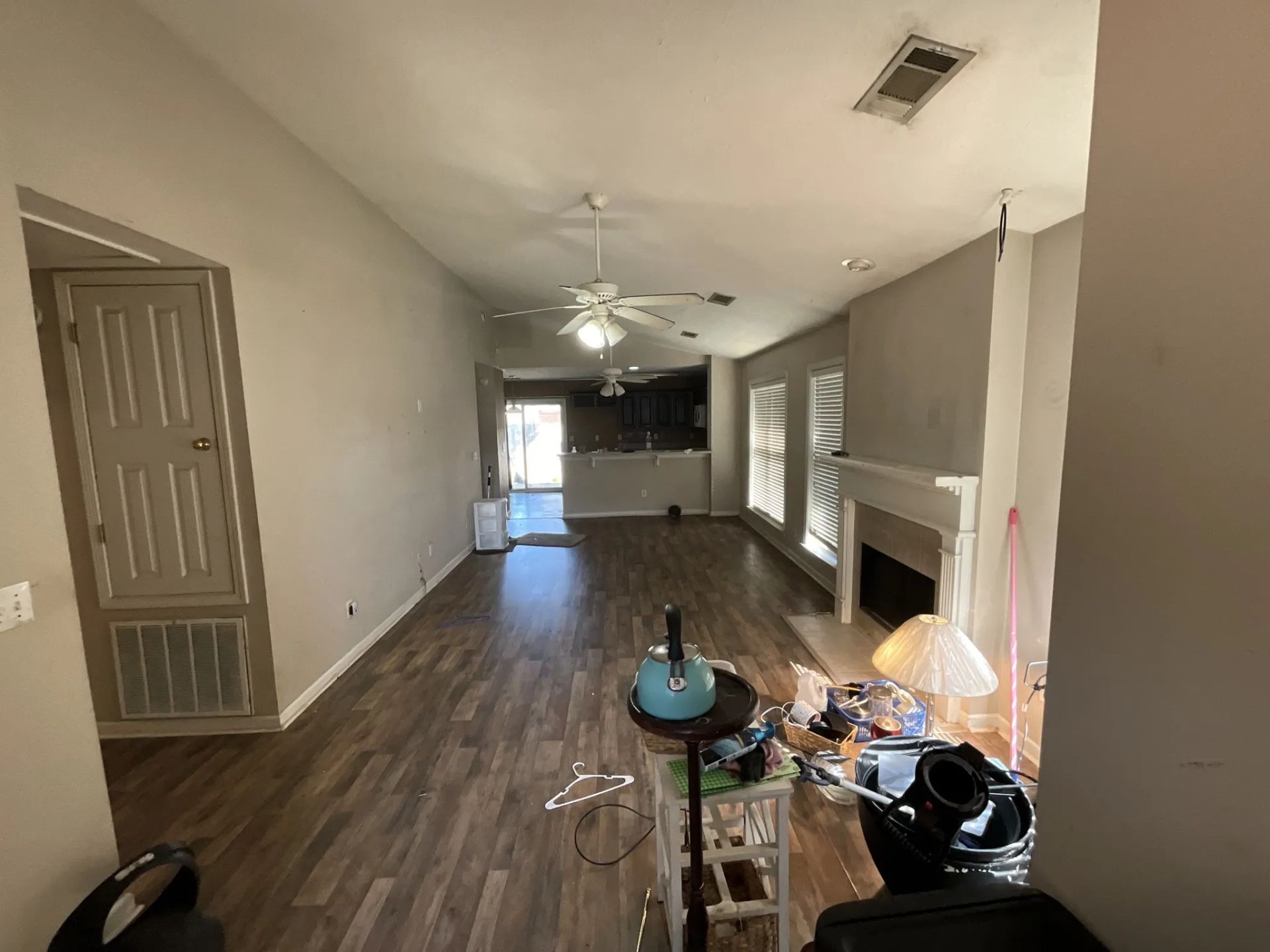 Empty living room with wood floors, fireplace, and open kitchen.