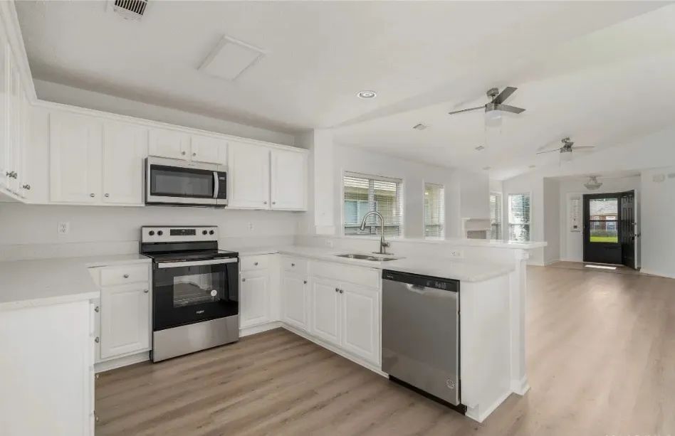 White kitchen with stainless steel appliances, white cabinets, and light wood flooring.