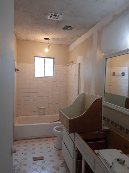 Bathroom undergoing renovation: tub, toilet, vanity, partially removed fixtures, off-white and tan walls.