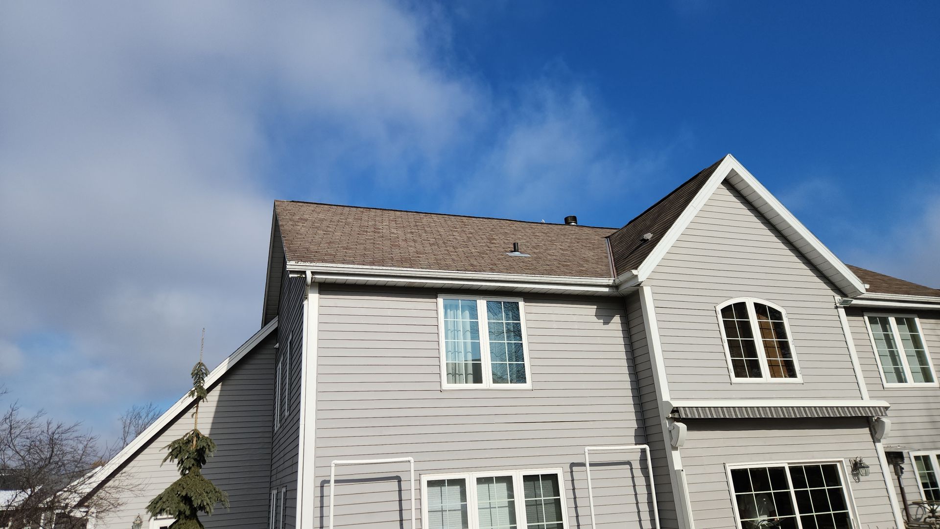 A large white house with a brown roof, new siding, and a blue sky in the background.