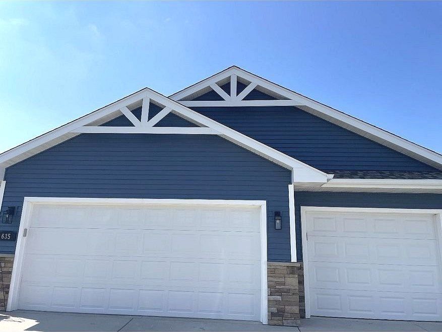 Blue house with white garage doors and decorative white roof accents, under a clear blue sky.