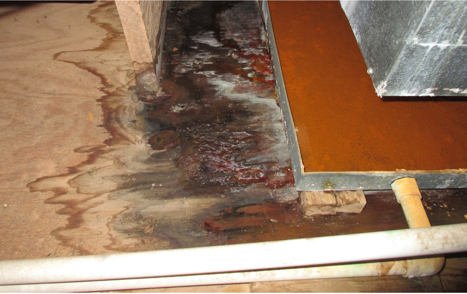 A piece of wood is sitting on a wooden floor next to a metal pipe.