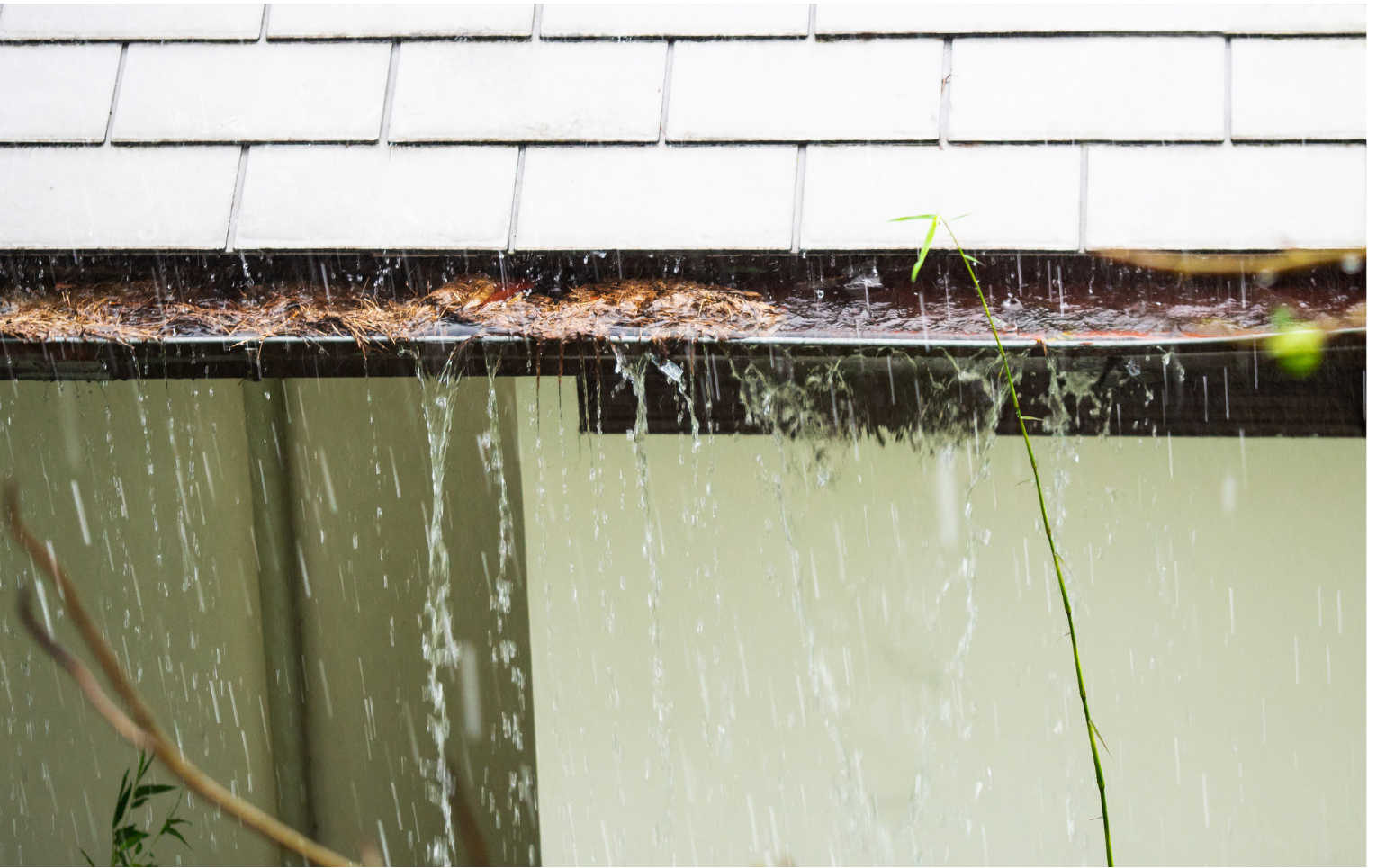 Rain is falling from the roof of a house into a gutter.