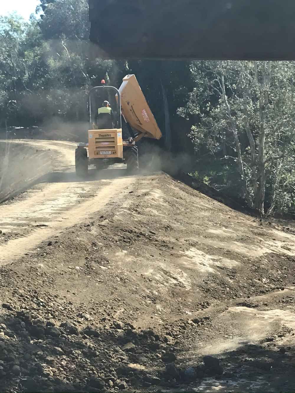 A Yellow Dump Truck is Driving Down a Dirt Road — Byron Earth & Road in Wardell, NSW