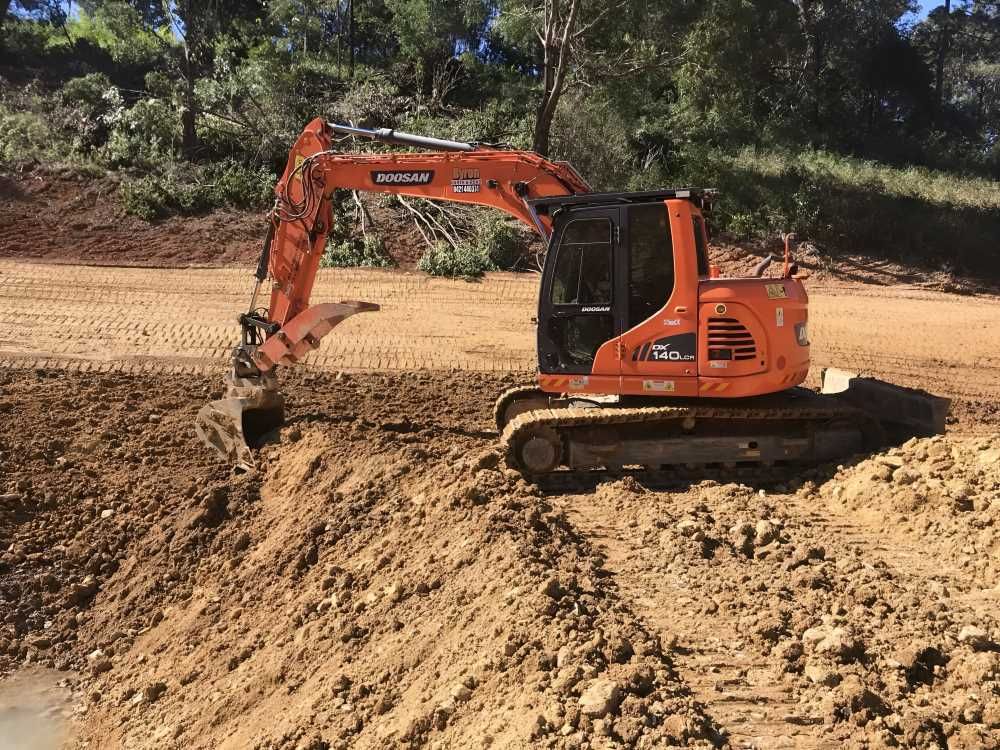 A Large Orange Excavator is Digging a Hole in the Dirt — Byron Earth & Road in Wardell, NSW