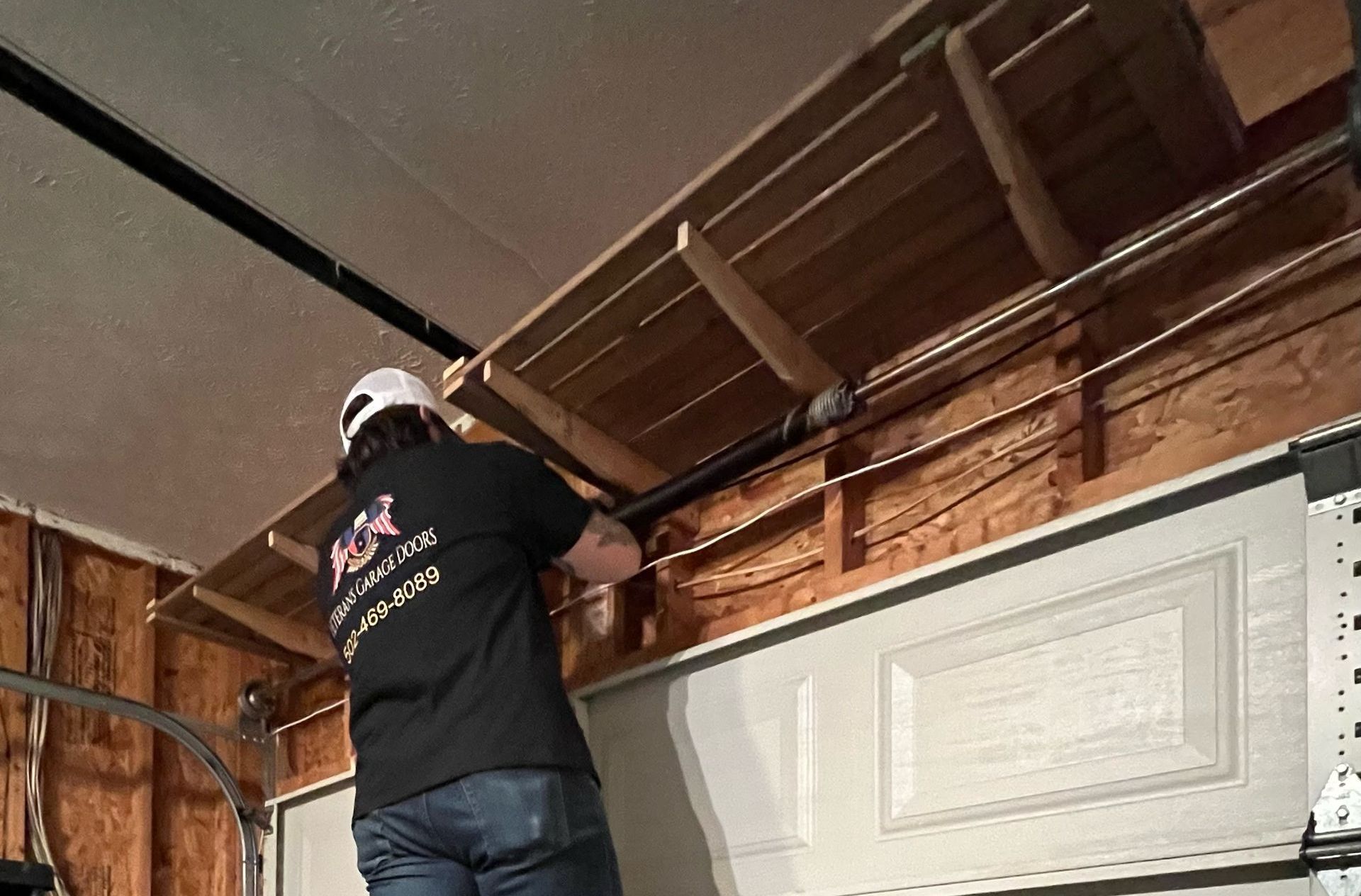 Person in a garage fixing a garage door, working near a wood frame and overhead track.
