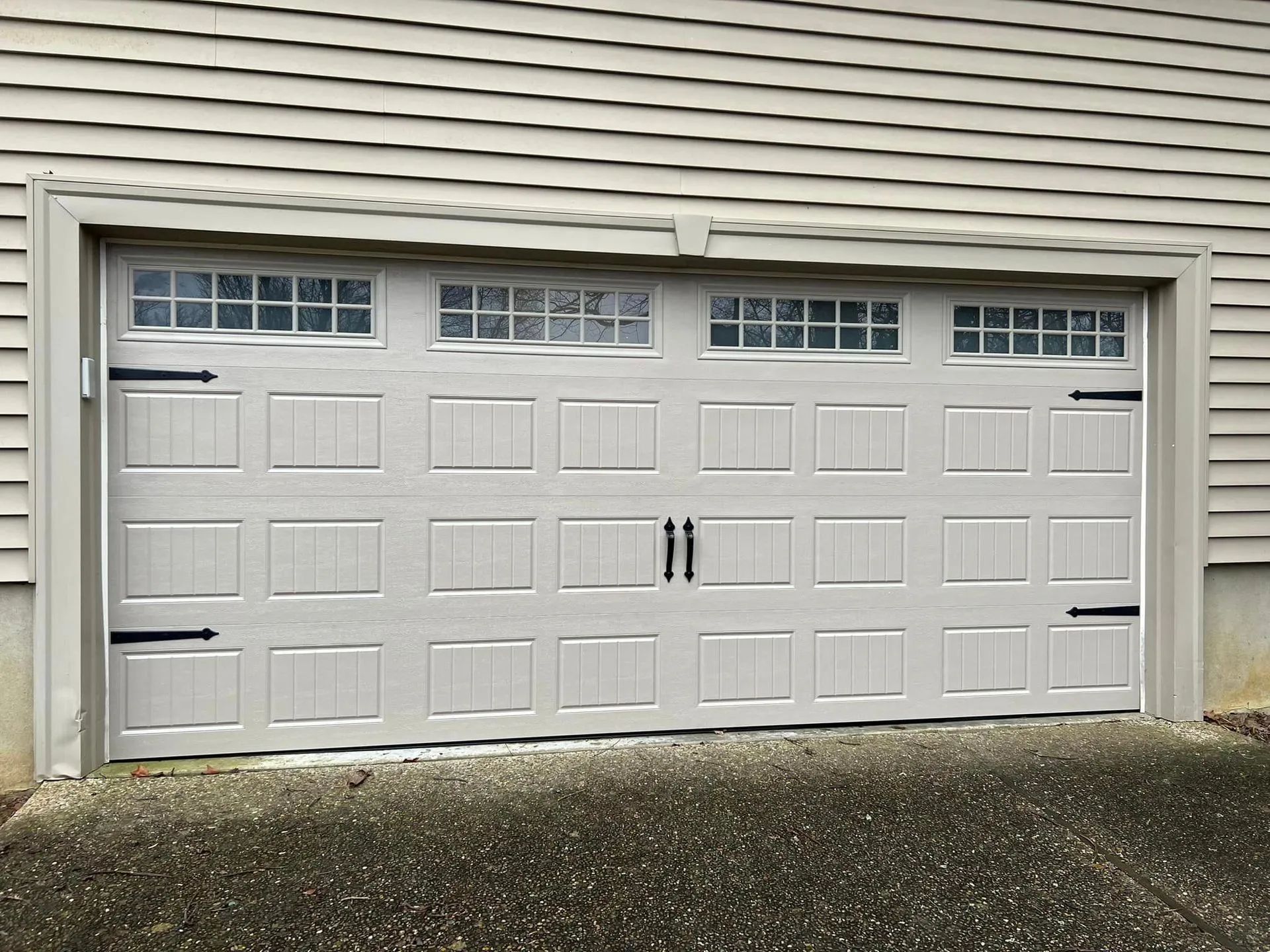 Closed light gray garage door with windows, black hardware, and light siding.