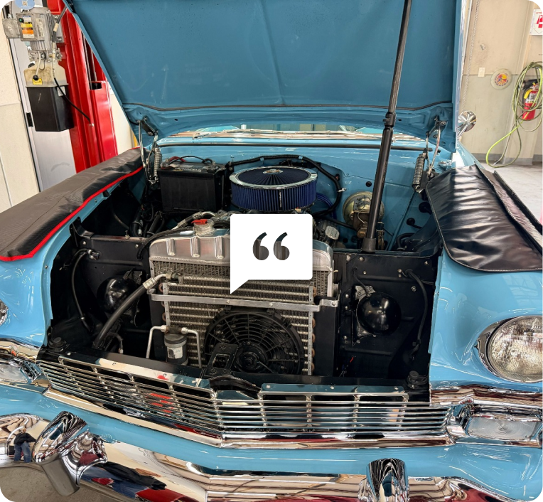 Light blue classic car with open hood, showing engine at an indoor showroom. | Motorvation Service Center