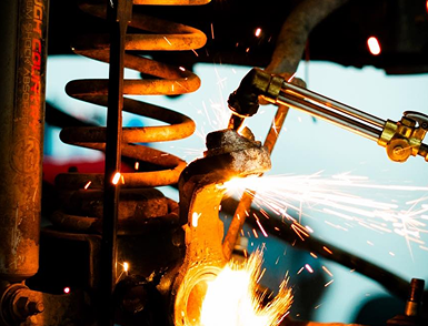 Metal grinding sparks fly in a workshop beside a large orange coil spring. | Motorvation Service Center