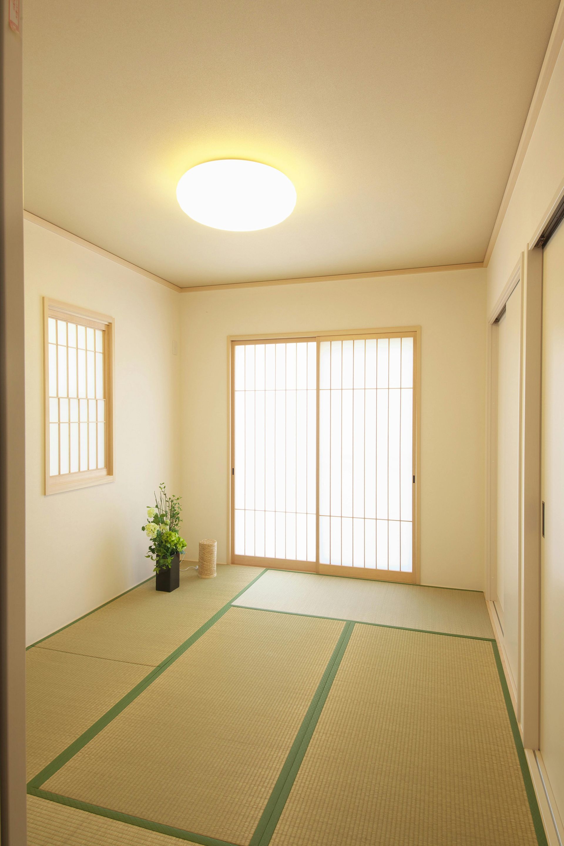Small Japanese-style room with tatami mats, a window, sliding door, and simple floral arrangement.