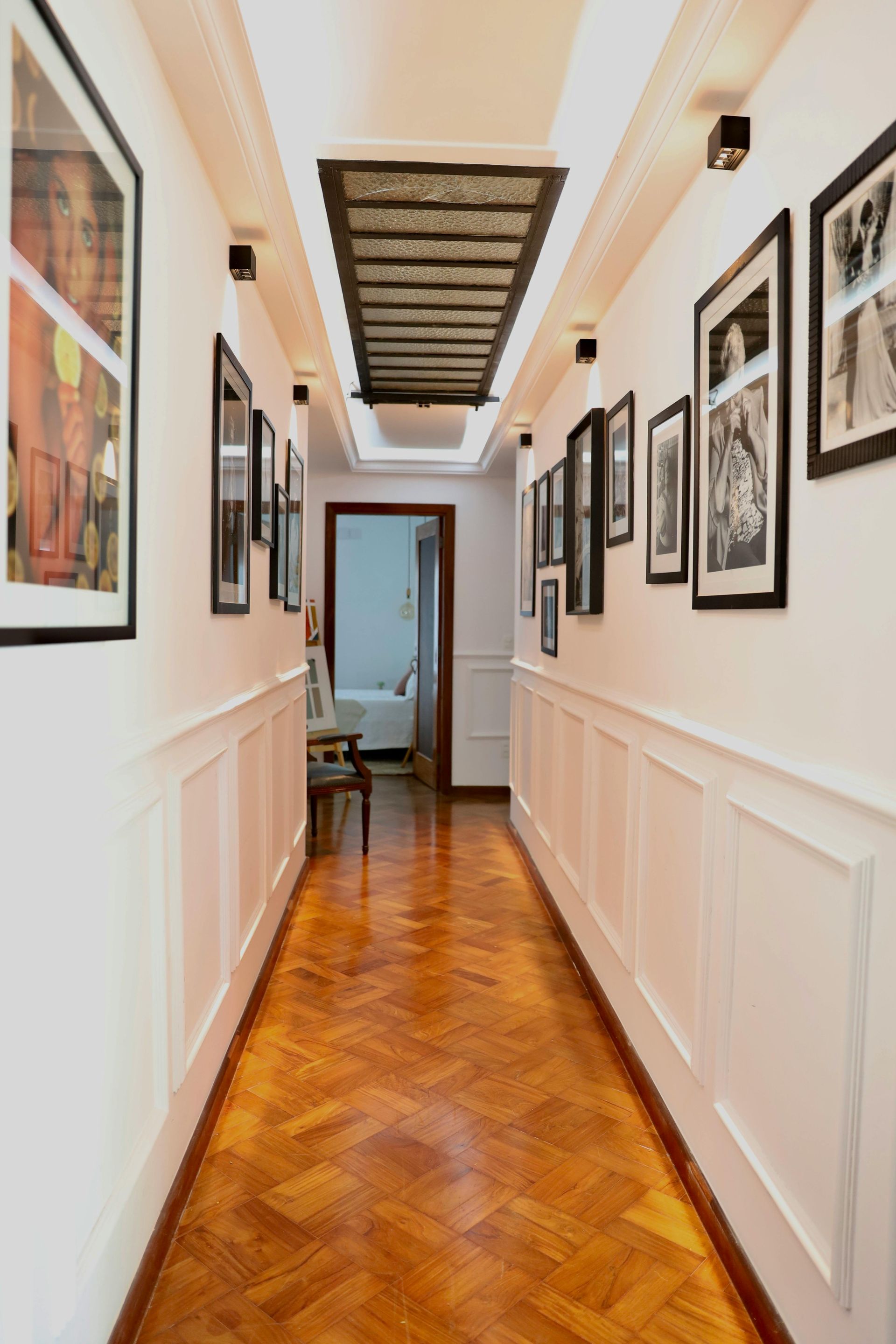 Long hallway with hardwood floors, framed photos, and a rectangular ceiling feature.