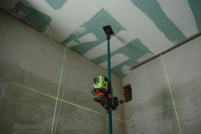 Green laser level projecting lines in room with unfinished drywall.