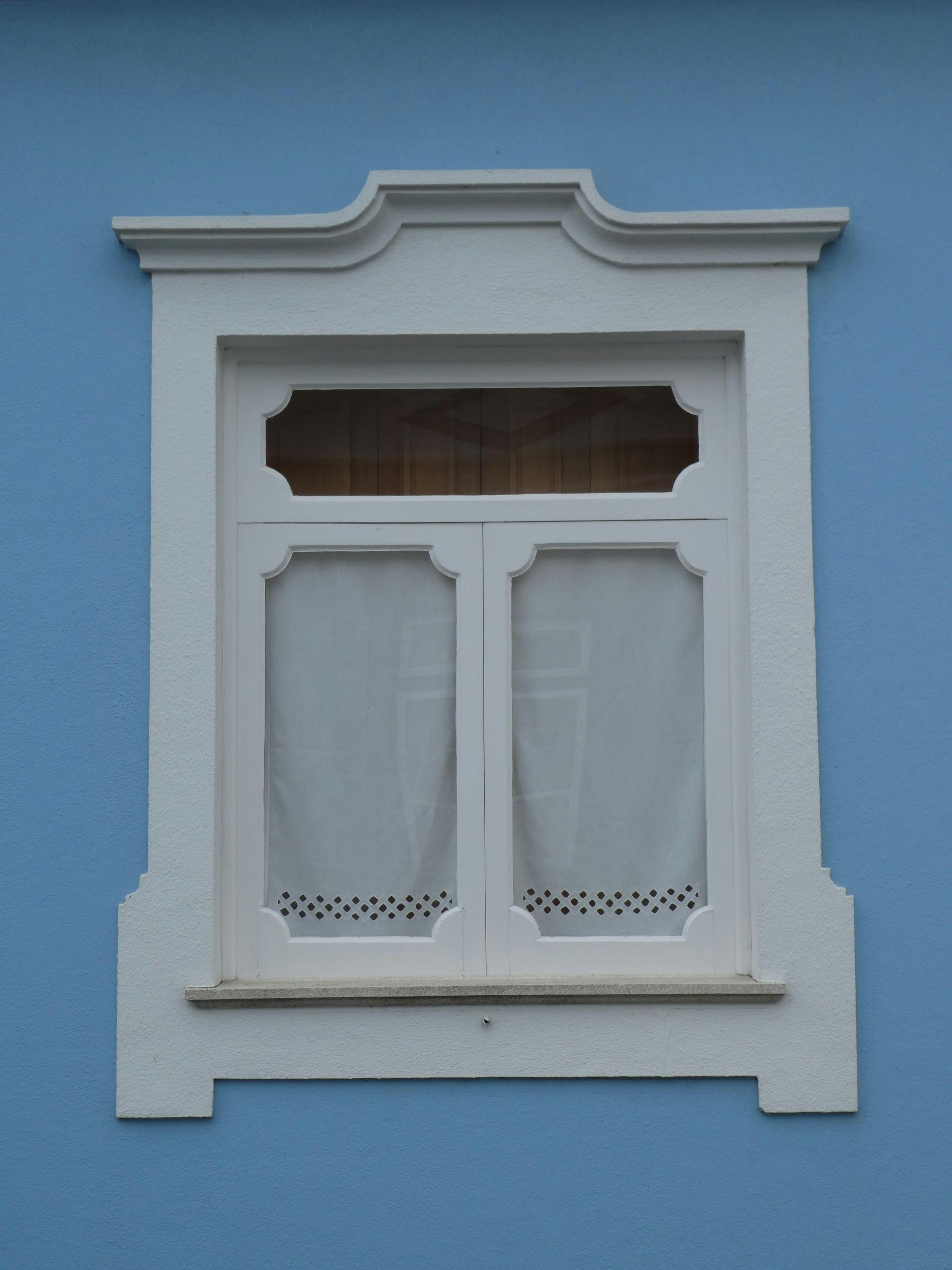 White-framed window with curtains on a blue wall.