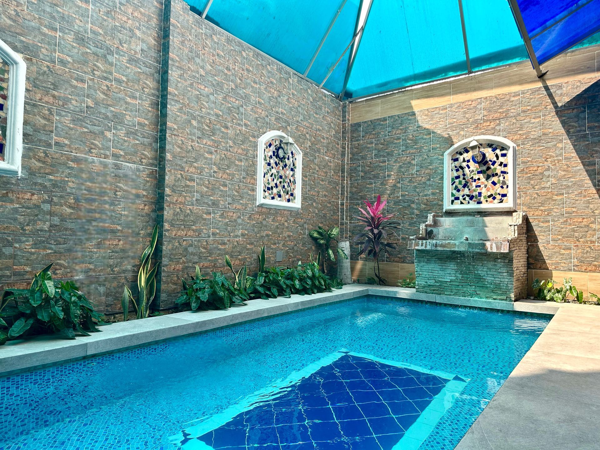 Una gran piscina rodeada por una pared de ladrillos y una sombrilla azul.