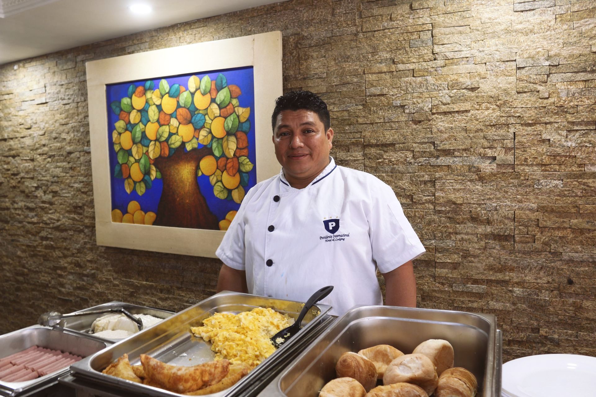 Un hombre con uniforme de chef está parado frente a una línea de buffet.