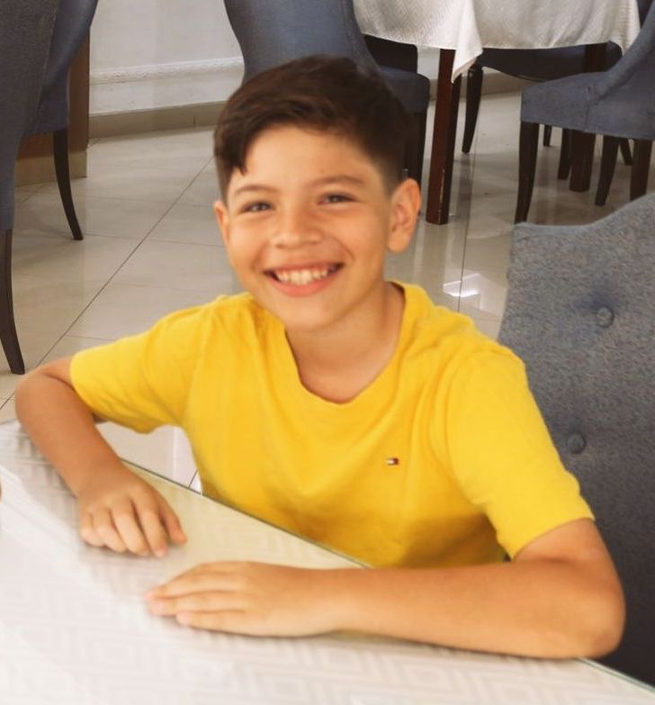 Un niño con una camisa amarilla sonríe mientras está sentado en una mesa.