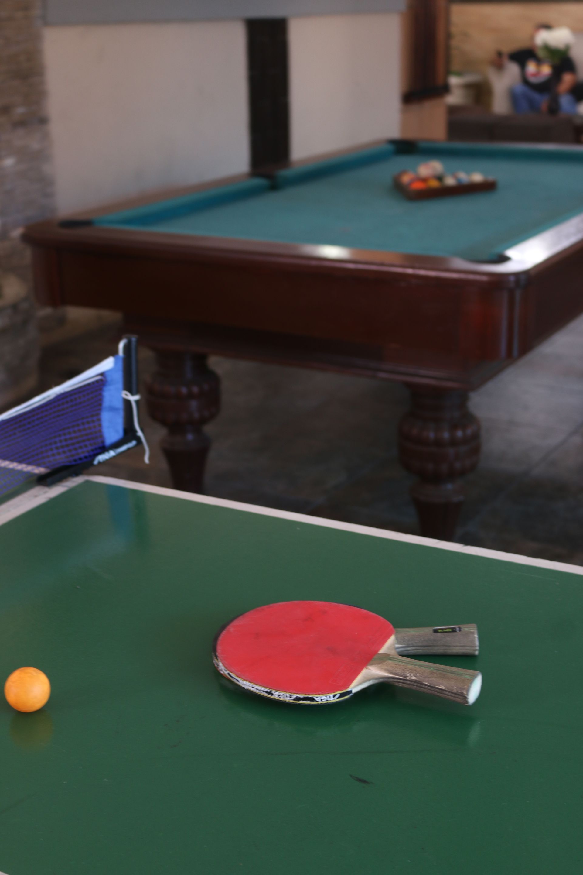 Raquetas de ping pong sobre una mesa frente a una mesa de billar