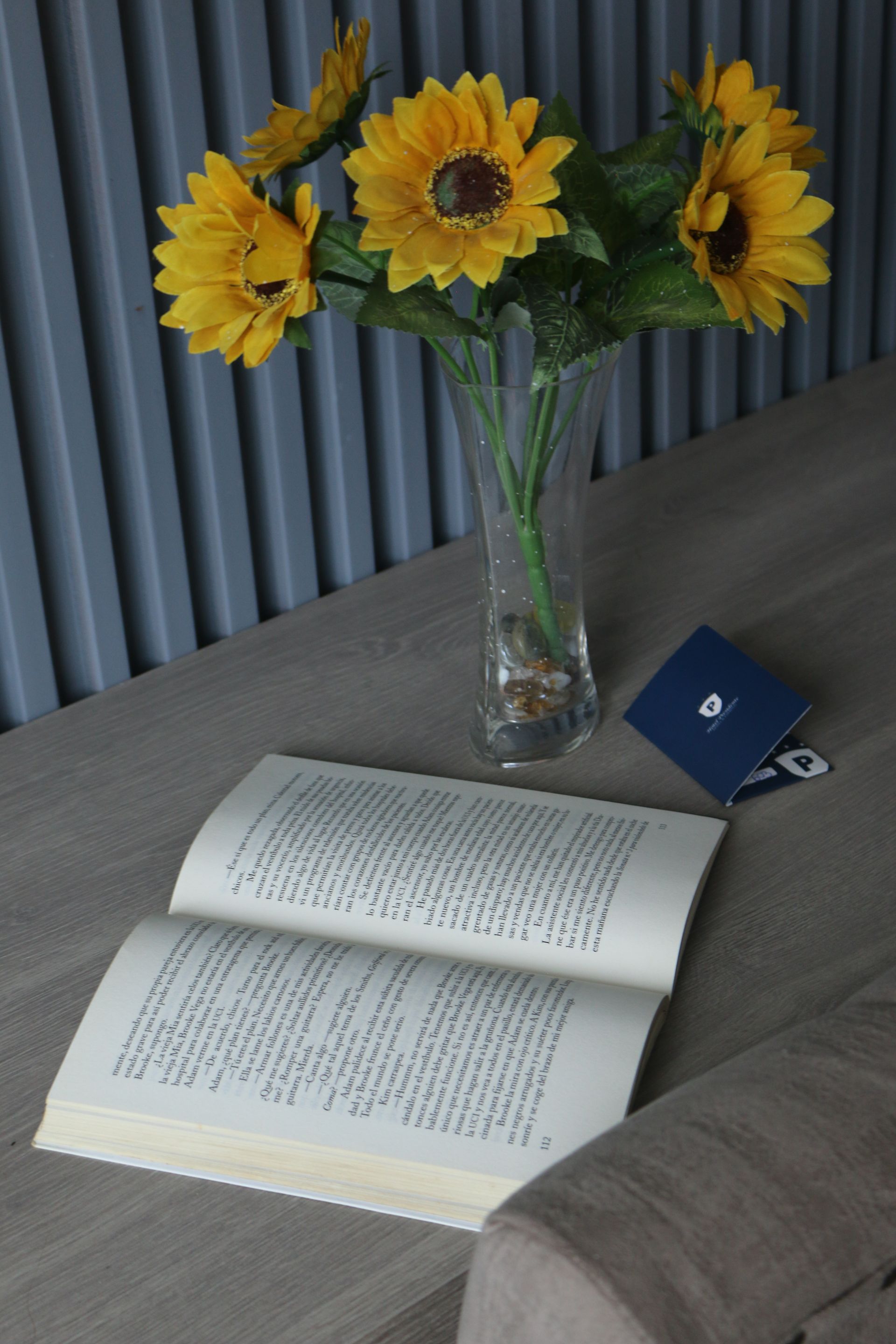 Un jarrón de girasoles reposa sobre una mesa junto a un libro abierto.